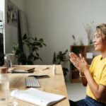 Woman smiling and clapping hands in a cozy home office environment.