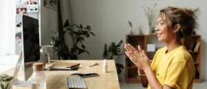 Woman smiling and clapping hands in a cozy home office environment.