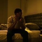 African American man sitting on a bed struggling with insomnia at night.