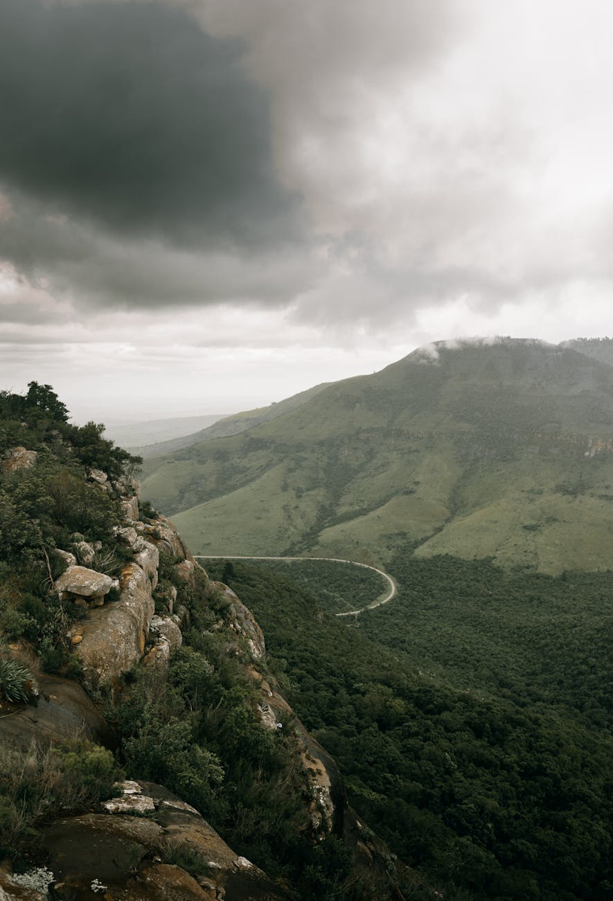 Dramatic aerial view of lush green mountains and a winding road under a cloudy sky.