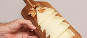 Close-up of cheese slices and walnuts on a wooden board held by a hand.