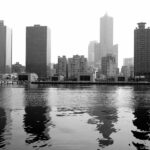 Black and white cityscape of Kaohsiung skyline with reflections on the water.