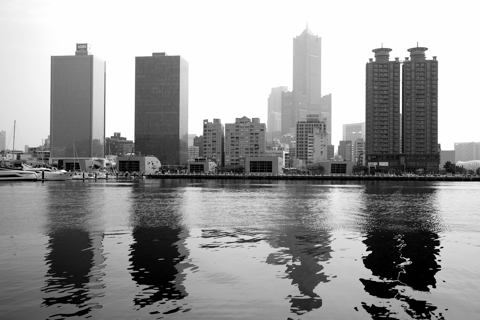 Black and white cityscape of Kaohsiung skyline with reflections on the water.